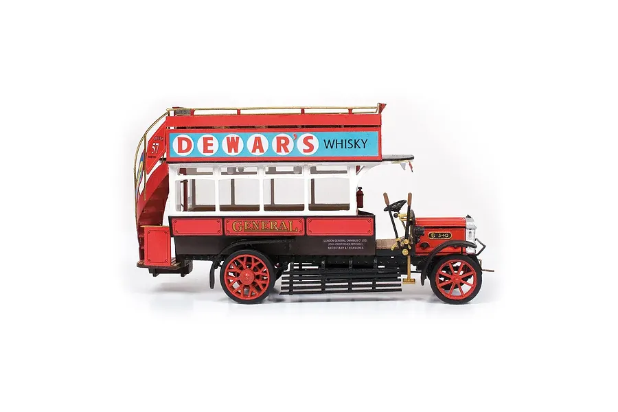 Side view of a completed OcCre 1/24 scale AEC B-Type London bus model, featuring red and white paint with Dewar's Whisky advertising signage.