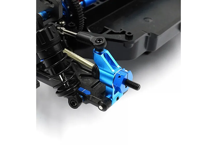 A close-up view of a blue anodized aluminium rear hub installed on an RC car chassis, showing the suspension arm and shock absorber connection.