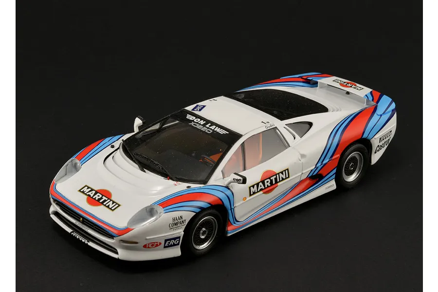 A high-angle studio shot of a 1/24 scale Jaguar XJ220 race car model with white, red, and blue Martini racing livery on a black background.