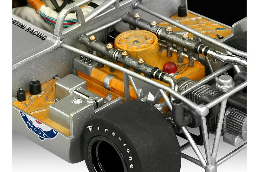 Close-up of a detailed scale model Porsche 917 race car engine bay with silver tubular chassis, orange engine block, and Firestone branded tires.