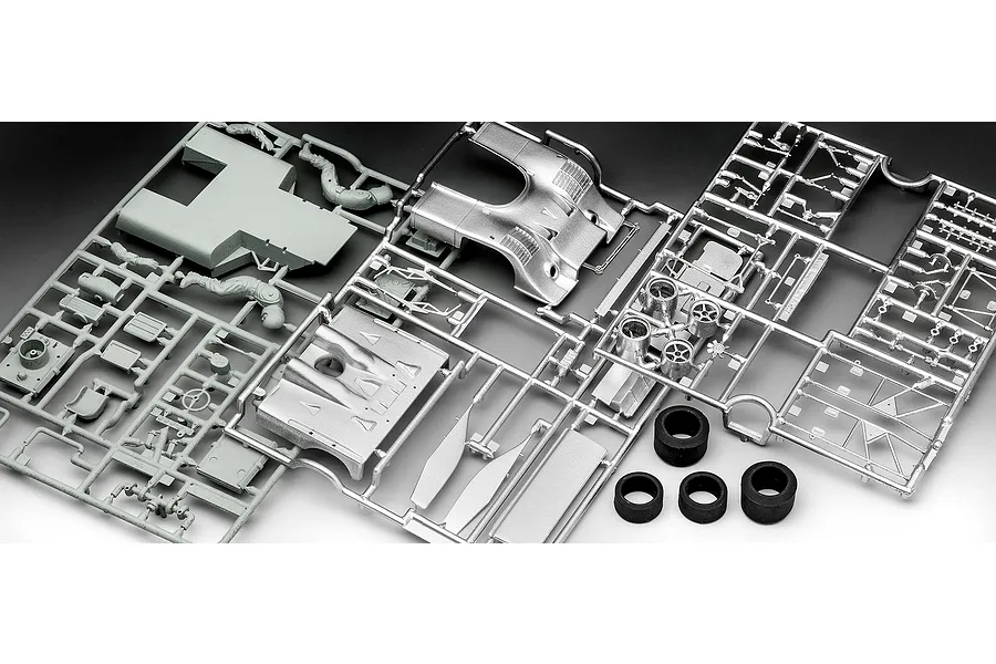 Plastic model kit sprues for a Porsche 917 race car including grey and chrome-plated parts and four black rubber tires.