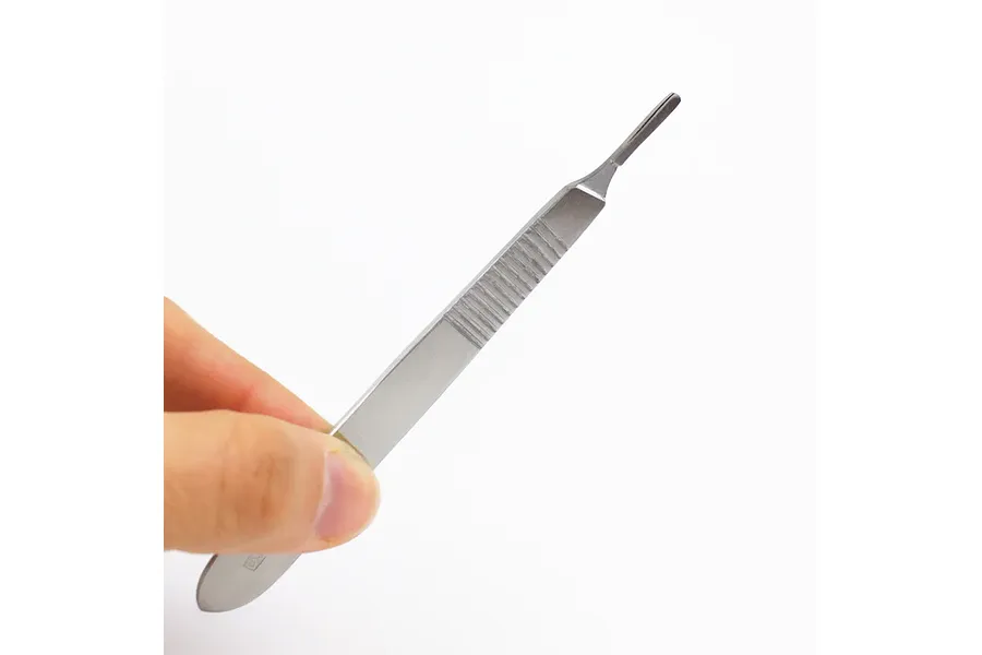 A hand holding a stainless steel #3 scalpel handle against a plain white background.