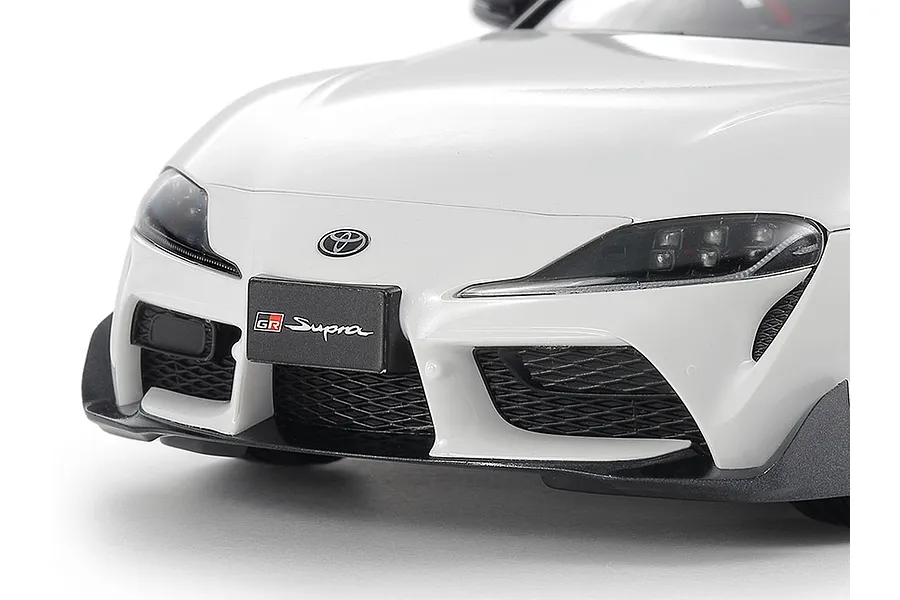Close-up of the front bumper and headlights of a white Tamiya 1/24 scale Toyota GR Supra plastic model car kit.