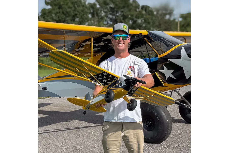 A man holding a HobbyZone Carbon Cub S 2 RC plane in front of a full-sized matching aircraft.