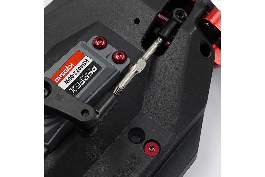 Close-up of a metal turnbuckle installed on an RC car chassis, connecting a Kyosho servo to the steering assembly.