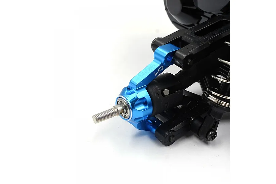 Close-up of a blue anodized aluminium RC steering knuckle installed on a black plastic suspension arm against a white background.