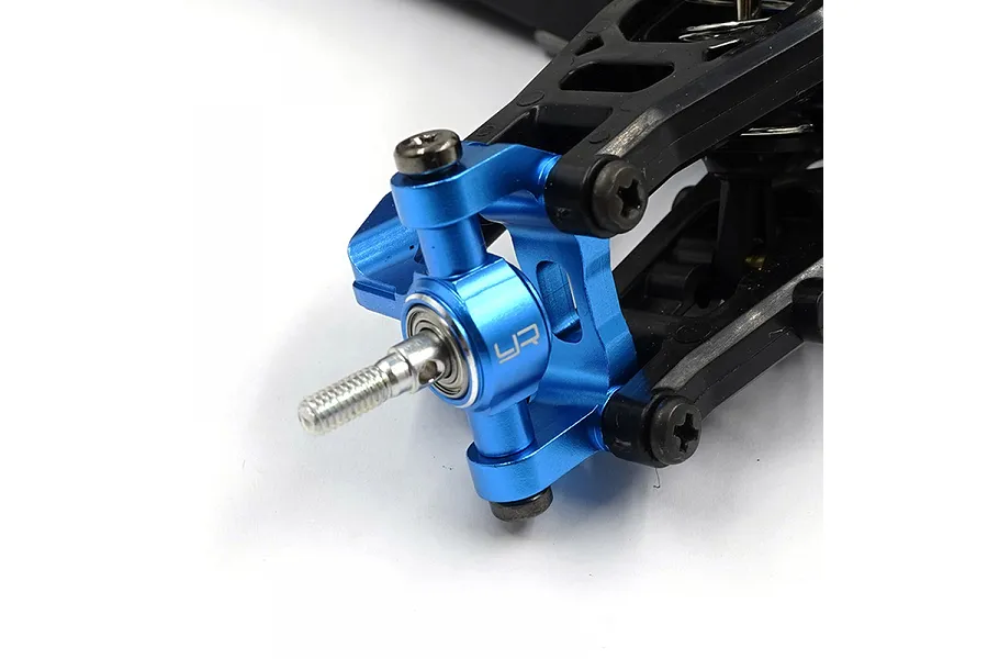 Close-up of a blue anodized aluminium RC steering knuckle installed on a black plastic suspension arm.