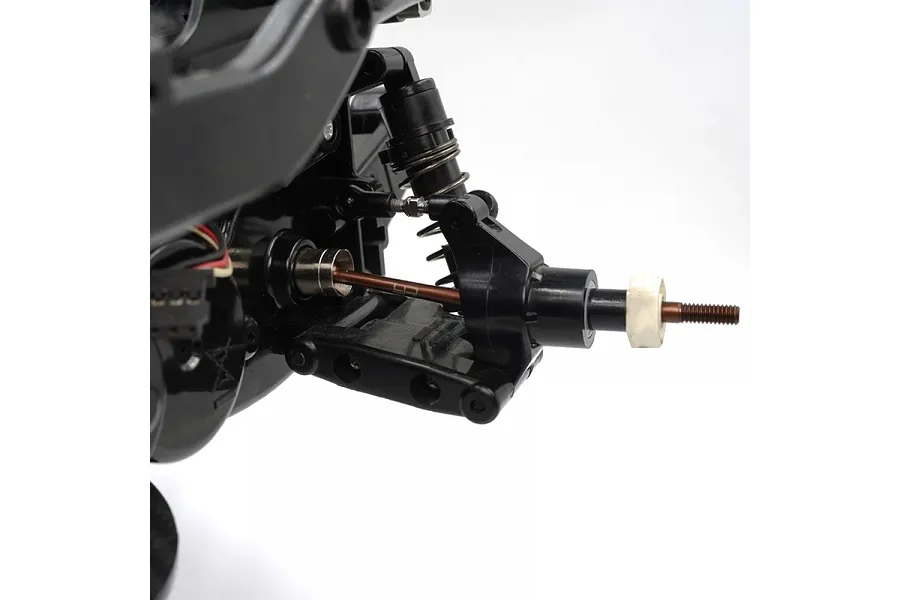 Close-up of an RC car suspension assembly showing a brown spring steel CVD driveshaft installed on a black plastic chassis.