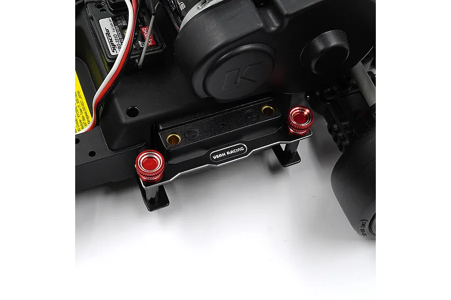 A close-up of a Yeah Racing aluminium battery hold-down set installed on a black RC car chassis, featuring black brackets and red knurled thumb nuts.