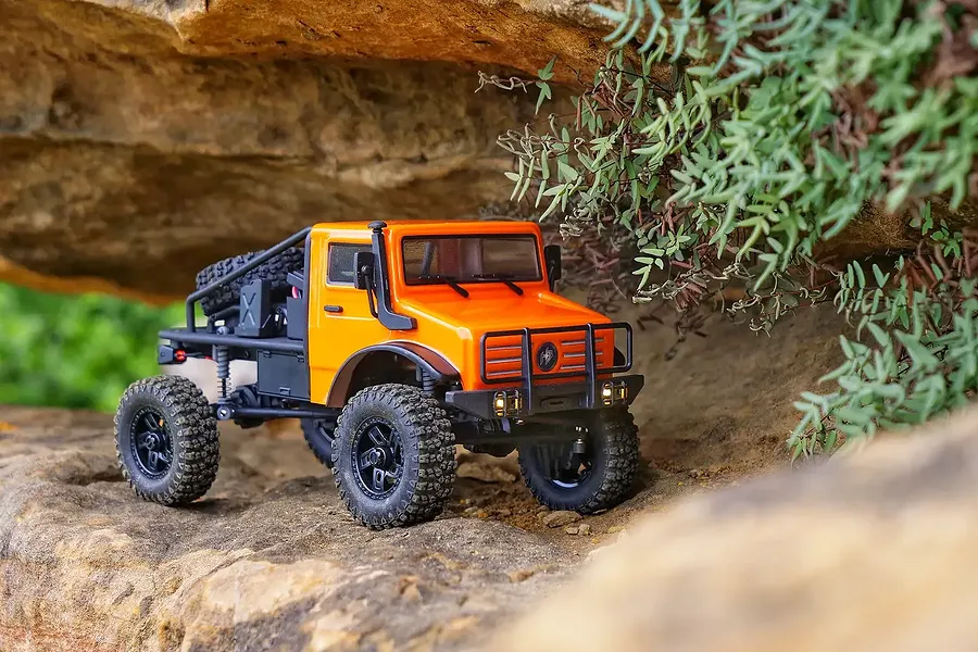 Orange Hobby Plus CR-18P Evo Trail Hunter RC rock crawler driving on rocky terrain under a rock ledge.