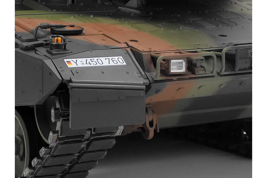 Close-up of the front hull of a Tamiya Leopard 2 A7V RC tank model, showing camouflage paint, German license plate decal, and headlight detail.