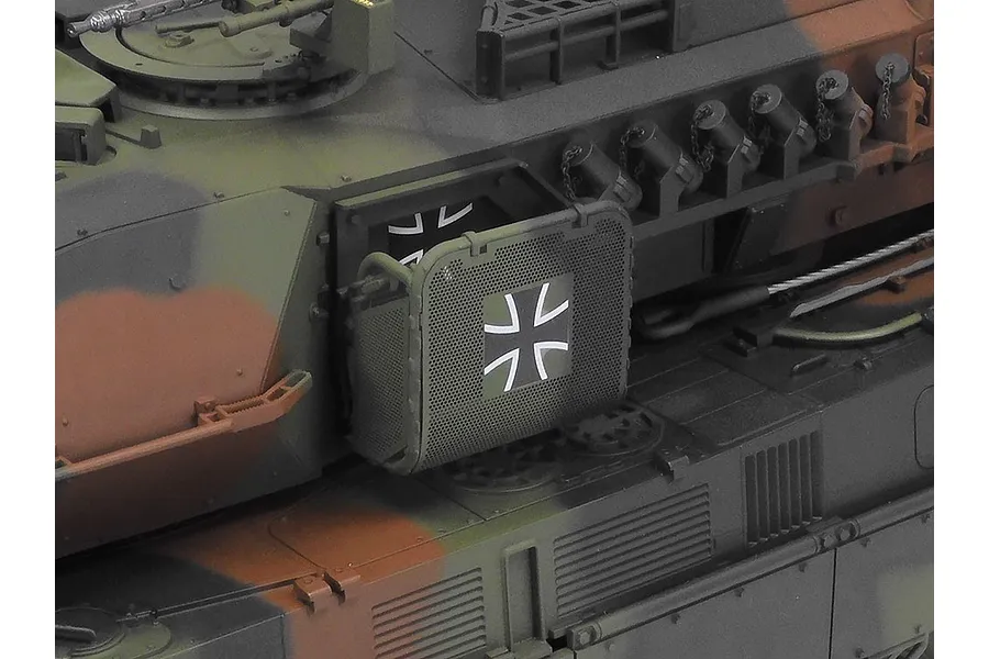 Close-up of the side turret detail on a Tamiya Leopard 2 A7V RC tank model, featuring a German Iron Cross emblem on a mesh storage bin.