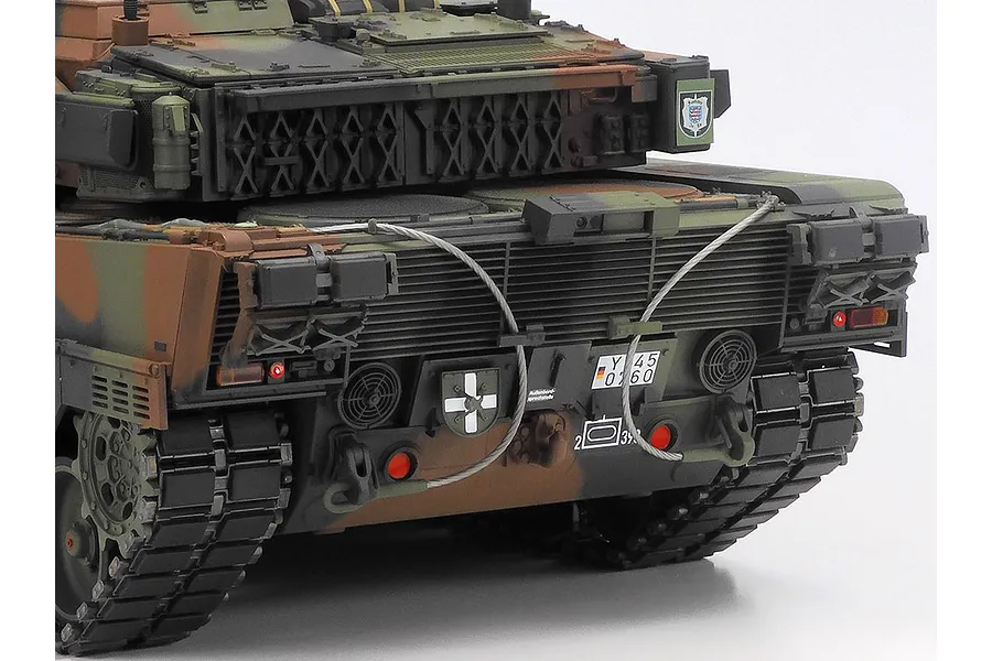 Rear view of a detailed Tamiya Leopard 2 A7V RC tank model featuring camouflage paint, tow cables, and German military markings.