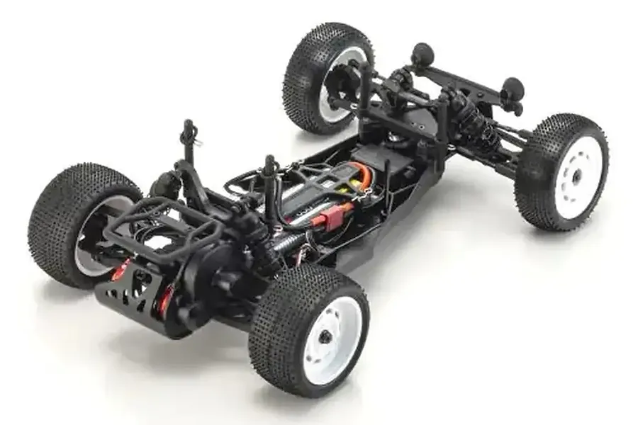 A high-angle studio shot of the Kyosho Ultima SB Dune Master 1/10 scale 2WD RC buggy chassis, showing the black frame, white wheels, and off-road tires.