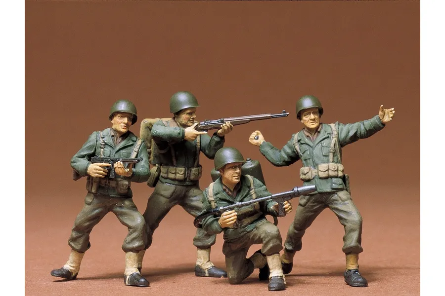 Four painted 1/35 scale Tamiya U.S. Army infantry model figures in various combat poses against a brown background.