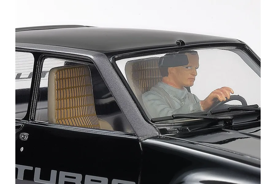 Close-up of a 1/24 scale Renault 5 Turbo model car interior showing a painted driver figure behind the steering wheel and tan patterned seats.