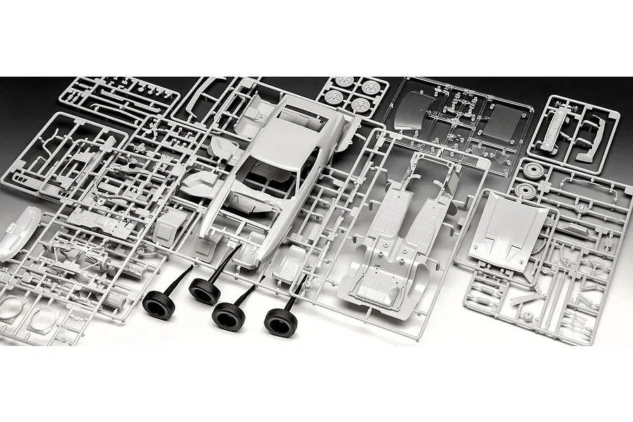 Unassembled grey plastic model car parts on sprues for a 1971 Ford Mustang Boss 351, including the car body, chassis, and four black rubber tires.