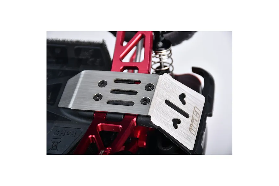 A stainless steel skid plate installed on the front of an RC car chassis with red aluminum suspension arms.
