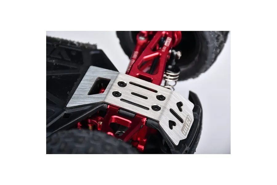 A stainless steel skid plate installed on the underside of an RC car chassis, showing red aluminum suspension components and black tires.