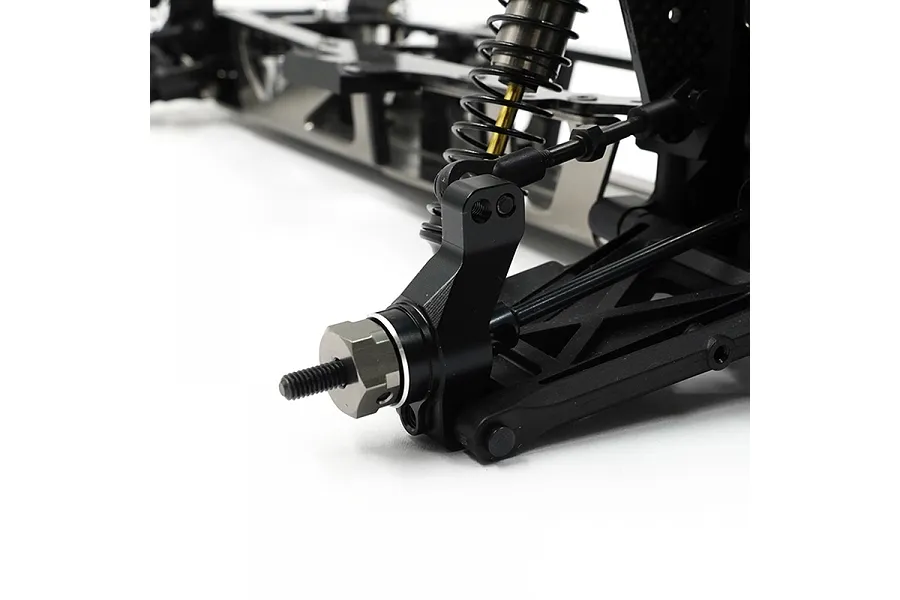 Close-up of a black aluminium rear hub installed on an RC car chassis, showing the suspension arm, shock absorber, and wheel hex nut.