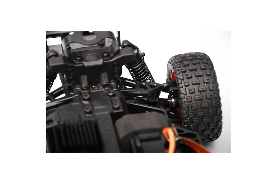 Close-up of a GPM Racing driveshaft installed on an RC car chassis, showing the metal shaft with branding and the surrounding suspension components.