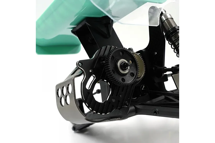 Close-up of a black aluminium motor mount and gear assembly installed on an RC car chassis with a teal wing visible in the background.