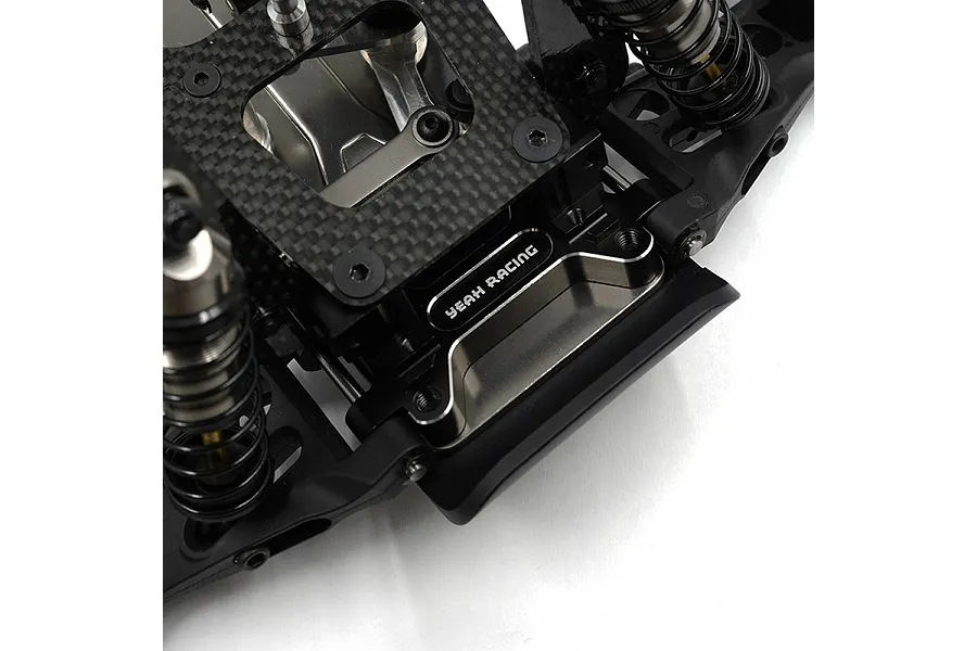 Close-up of a black aluminium Yeah Racing RC chassis component installed on a carbon fibre plate with suspension parts.
