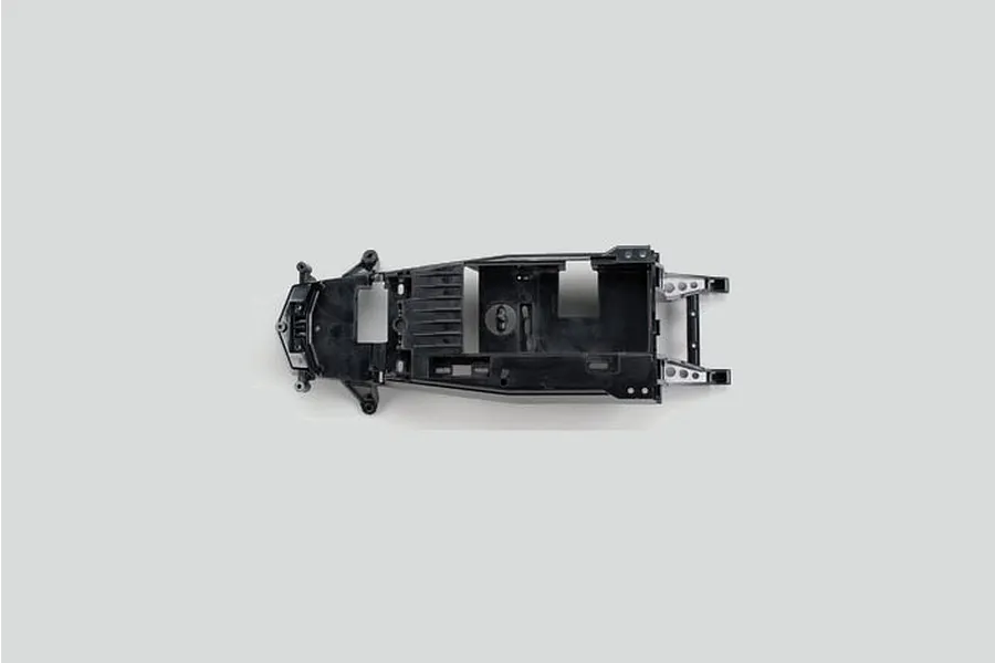 A top-down view of a black Tamiya RC main chassis component on a plain light grey background.