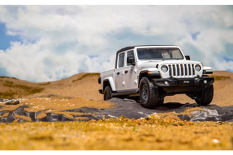 A white Jeep Gladiator model truck parked on a rocky, sandy terrain against a cloudy sky.