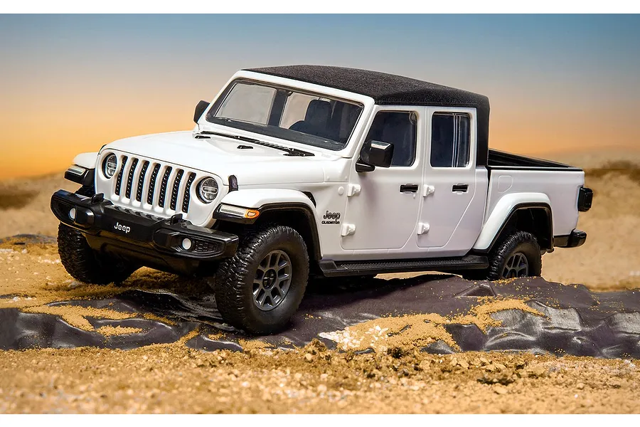 A white Jeep Gladiator model truck driving over a rocky, sandy terrain with a sunset background.