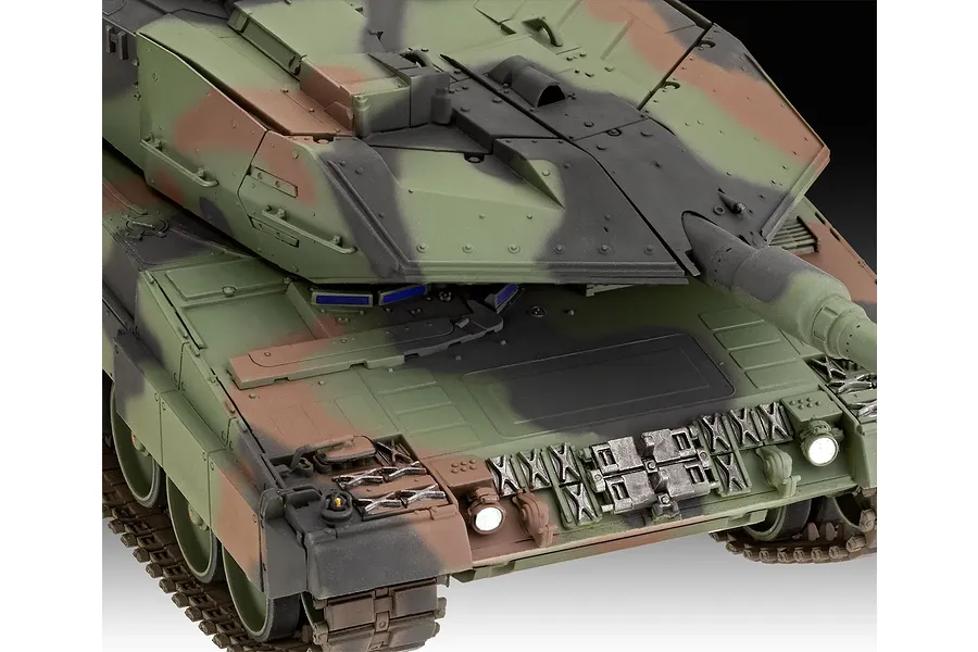 Close-up of a 1/35 scale model of a Leopard 2A6M+ tank, showing the turret, main gun, and front hull with detailed camouflage paint.