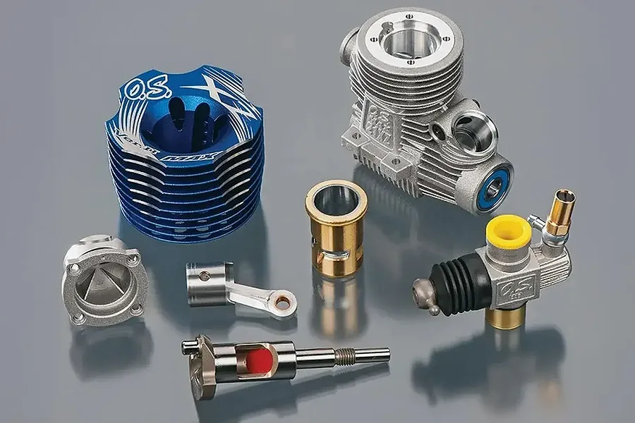 Disassembled parts of an O.S. Engines Max 21XZ-B V2 nitro engine, including the cooling head, crankcase, piston, sleeve, crankshaft, and carburetor.