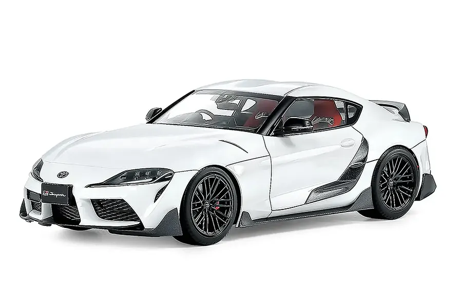 A studio shot of a white Tamiya 1/24 scale Toyota GR Supra model car with black wheels and carbon fiber style trim.