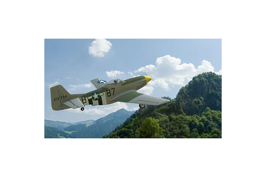 A digital rendering of a P-51 Mustang fighter plane flying over a mountainous landscape in the RealFlight simulator.