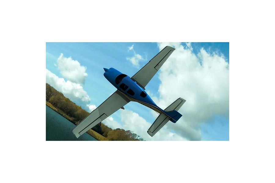 A digital rendering of a blue and white Cirrus SR22 aircraft flying over a lake and forest landscape in the RealFlight simulator.