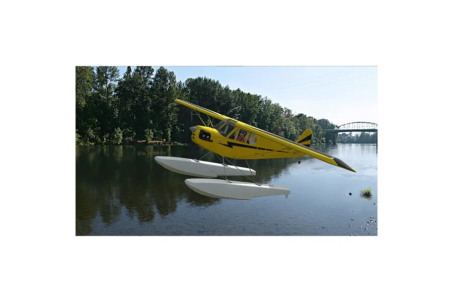 A yellow RC floatplane flying over a river in a digital simulation environment.
