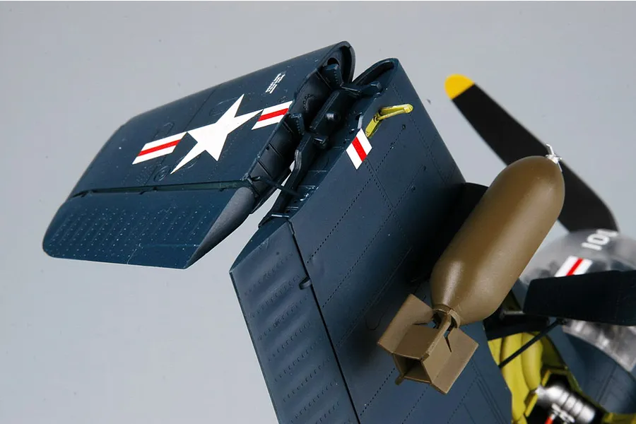 Close-up of a scale model aircraft wing with a folding mechanism and an attached bomb, featuring US military insignia.