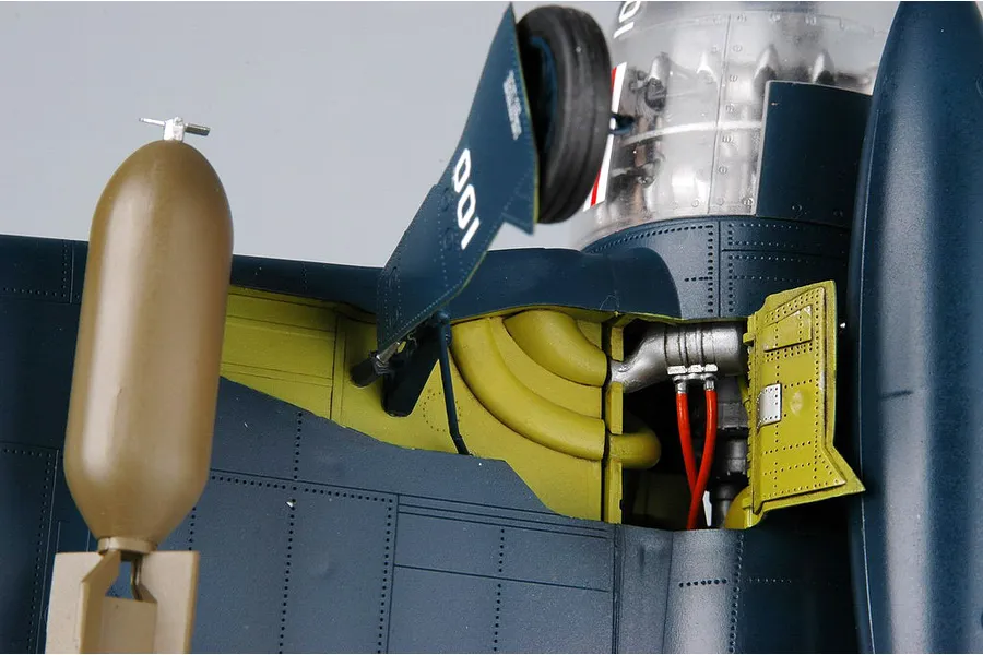 Close-up of a 1/32 scale model aircraft landing gear bay, showing detailed yellow interior, blue exterior panels, and a bomb mounted under the wing.