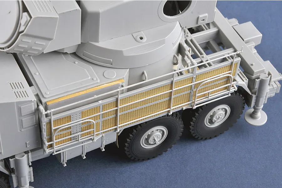 Close-up of a 1/35 scale plastic model of a Pantsir-S1 truck showing grey plastic chassis and gold-coloured photo-etched metal mesh side panels.