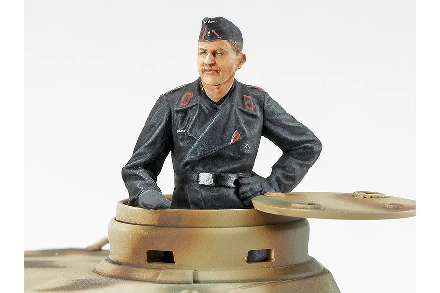 A painted 1/48 scale German tank commander figure emerging from the hatch of a camouflaged tank model.