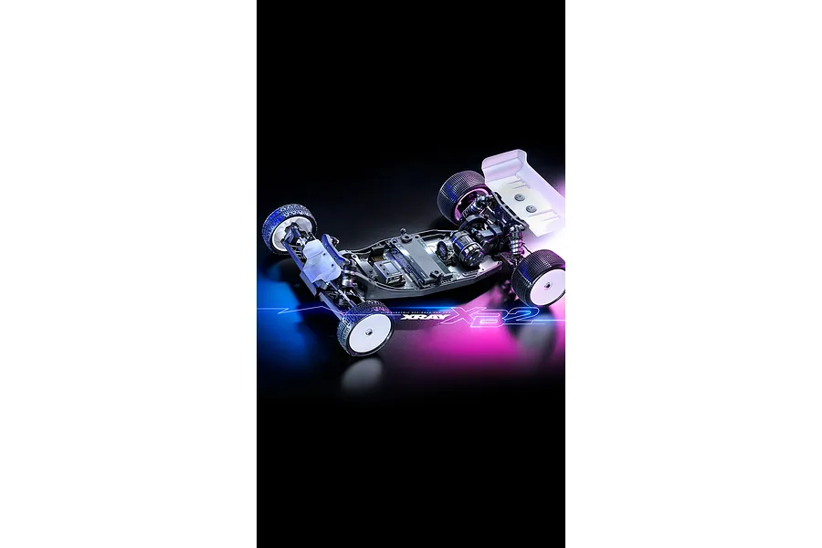 High-angle studio shot of an XRAY XB2'26 1/10 scale 2WD electric RC buggy chassis on a black background with blue and pink lighting effects.