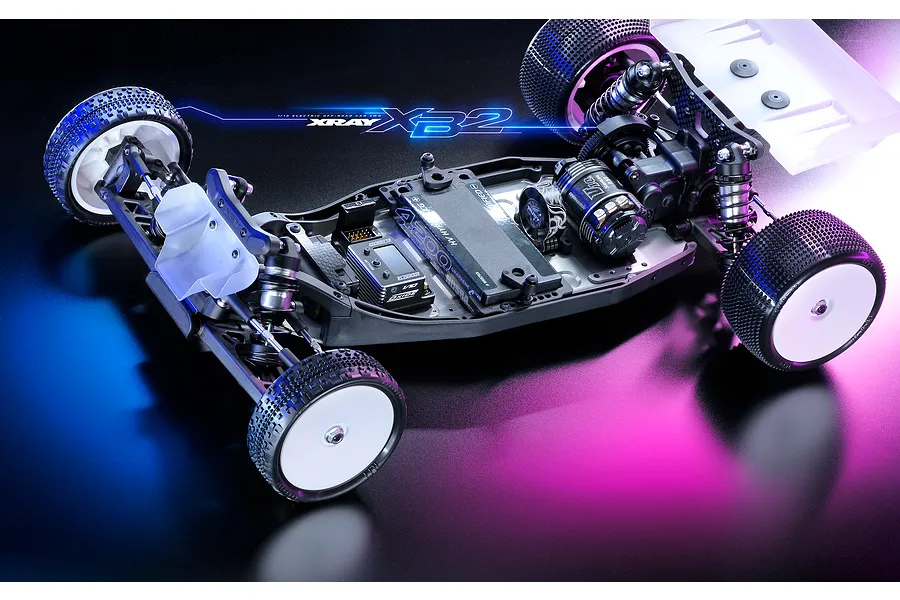 Studio shot of an assembled XRAY XB2 2WD RC buggy chassis on a dark reflective surface with blue and purple lighting.