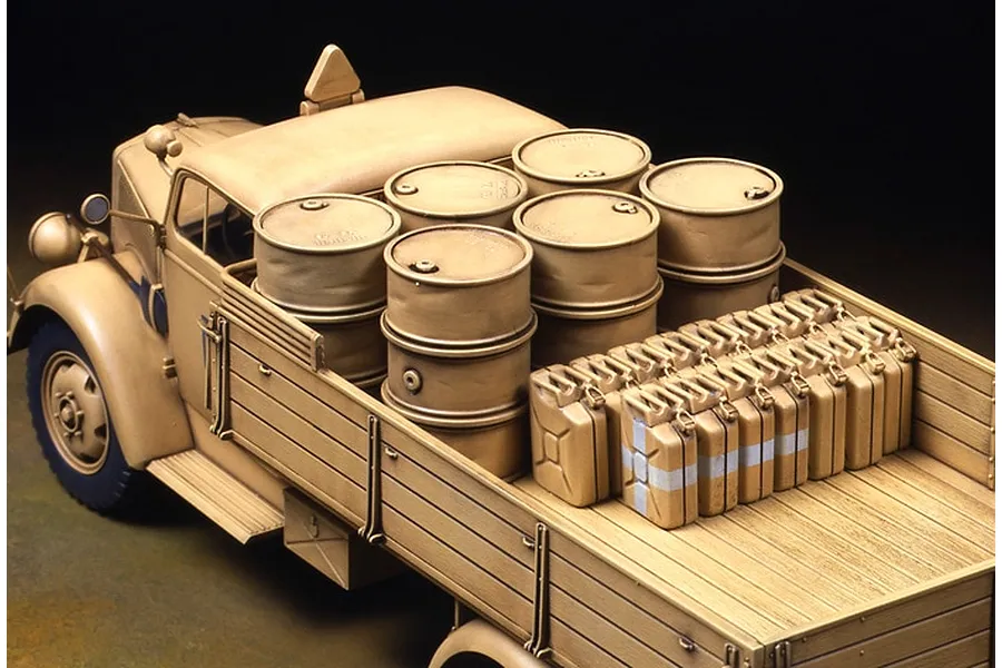 A 1/35 scale model of a German 3-ton cargo truck painted in tan, loaded with fuel drums and jerry cans in the truck bed.