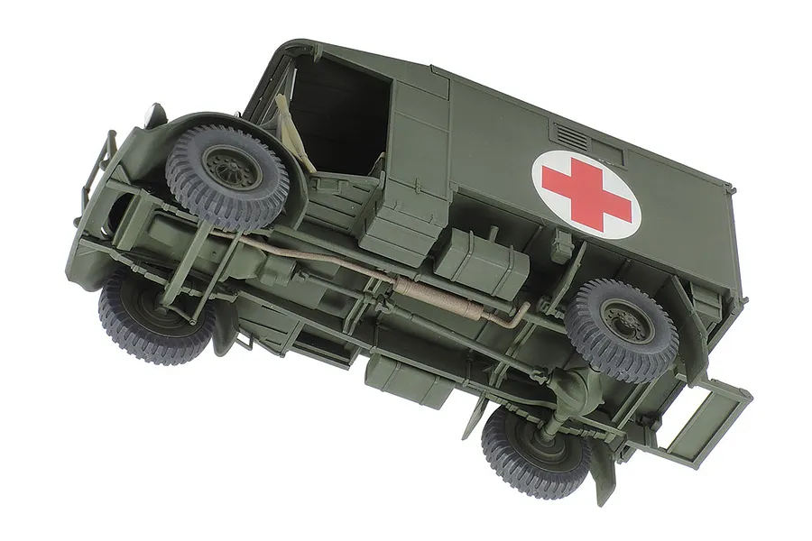 A low-angle view of an assembled and painted 1/48 scale Tamiya Austin K2 ambulance model, showing the chassis, wheels, and red cross emblem.