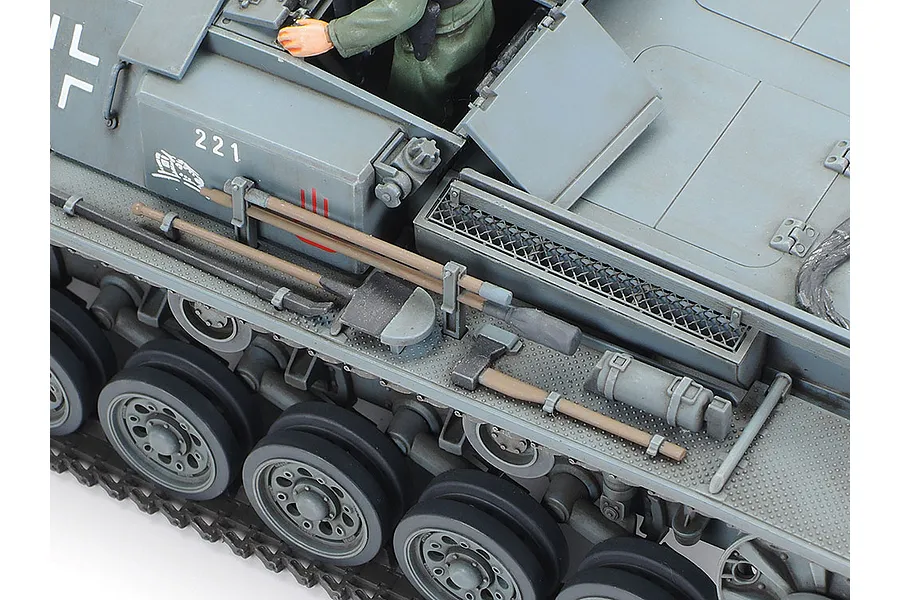 Close-up of a 1/35 scale Tamiya German Sturmgeschutz III model tank showing side hull details, tools, and a crew figure.