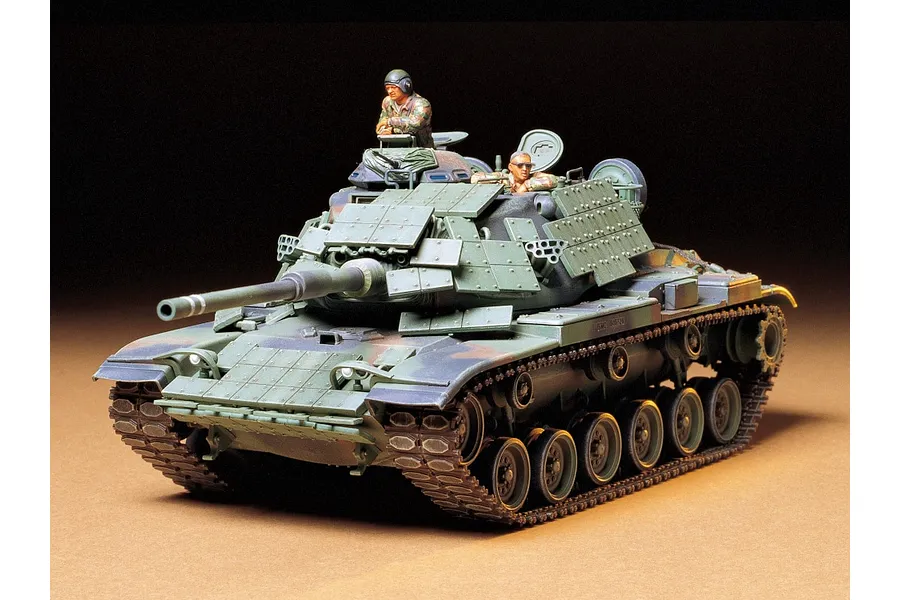 A fully assembled and painted 1/35 scale Tamiya M60A1 tank model with reactive armour, featuring two crew figures in the turret against a dark background.