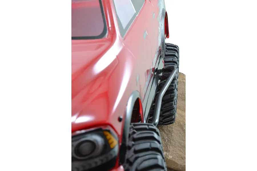 Close-up side view of a red RC truck body showing the black rock slider installed along the chassis above the off-road tires.