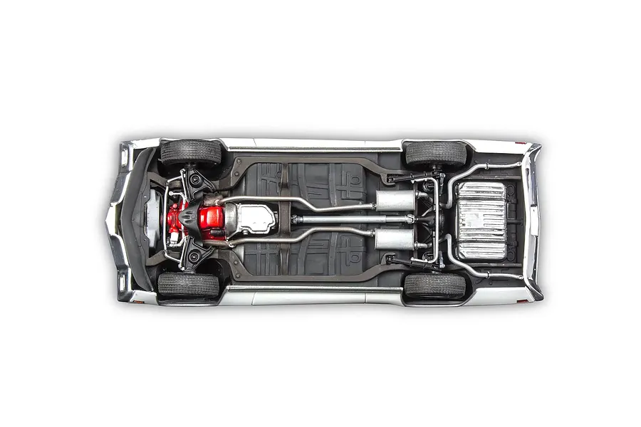 Underside view of a 1/24 scale plastic model car showing the chassis, drivetrain, exhaust system, and engine block.