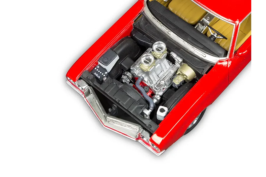 High-angle close-up of a red 1/24 scale model car engine bay with a detailed V8 engine, showing the radiator, battery, and tan interior.