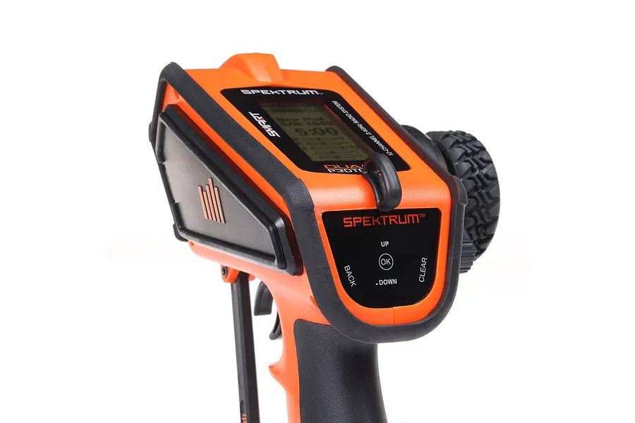 Close-up of the Spektrum DX Rugged orange RC transmitter showing the top control panel, display screen, and steering wheel.